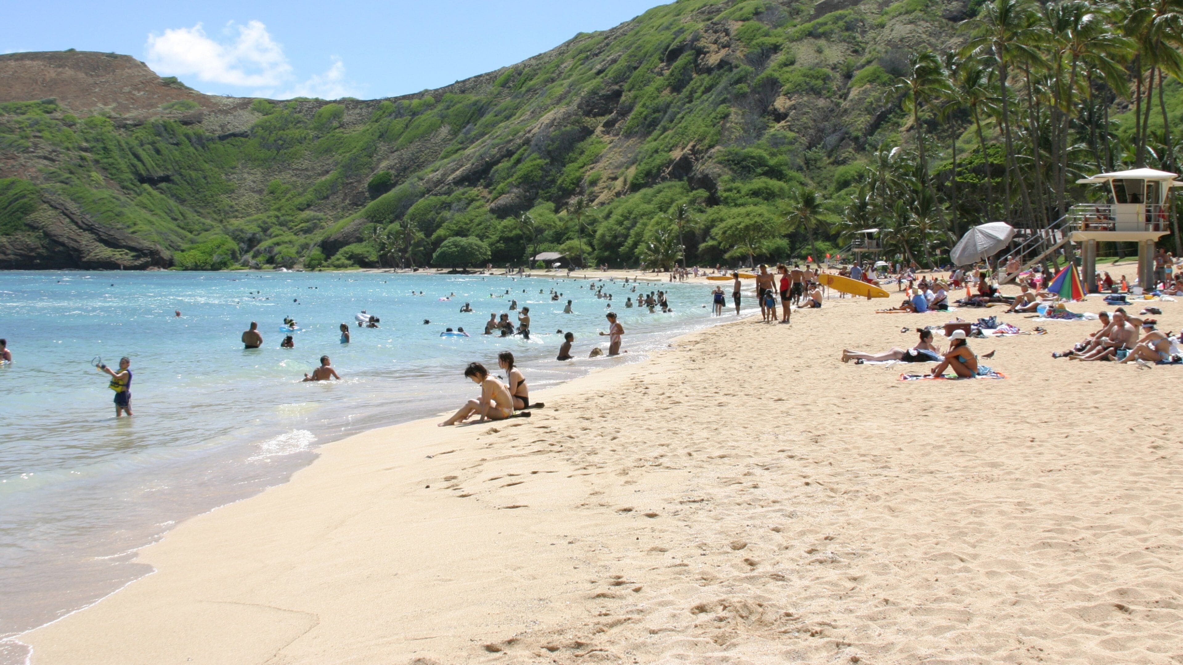 A crowded beach with people swimming and sunbathing.