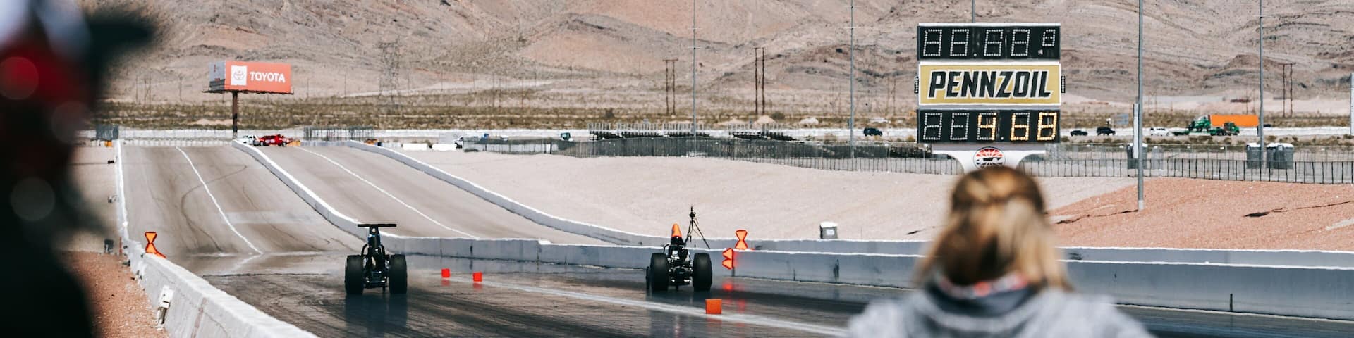 A desert racing track with a digital timer and a 'PENNZOIL' sign.