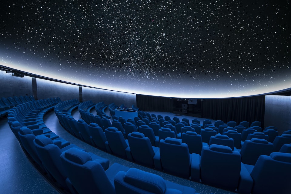 Un planétarium doté d’un dôme représentant un ciel étoilé et de rangées de sièges bleus.
