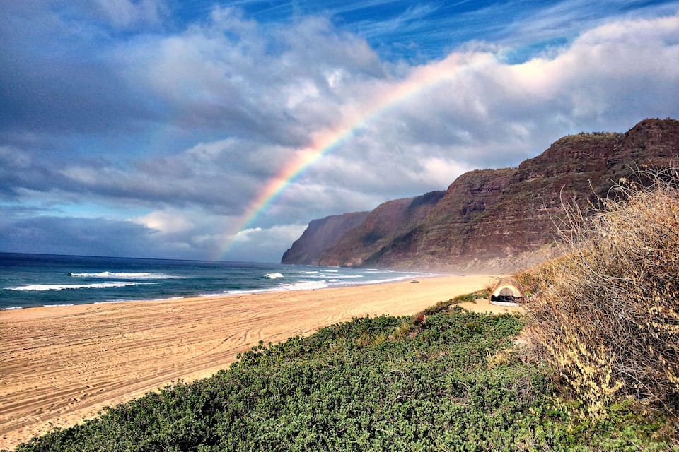 Une plage avec un arc-en-ciel, des vagues et une falaise.