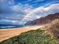 Ein Strand mit Regenbogen, Wellen und einer Klippe.