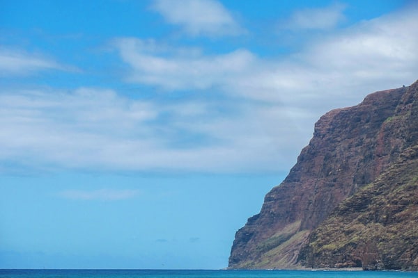 A coastal cliff with clear blue waters and a partly cloudy sky.
