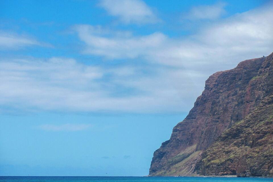 A coastal cliff with clear blue waters and a partly cloudy sky.