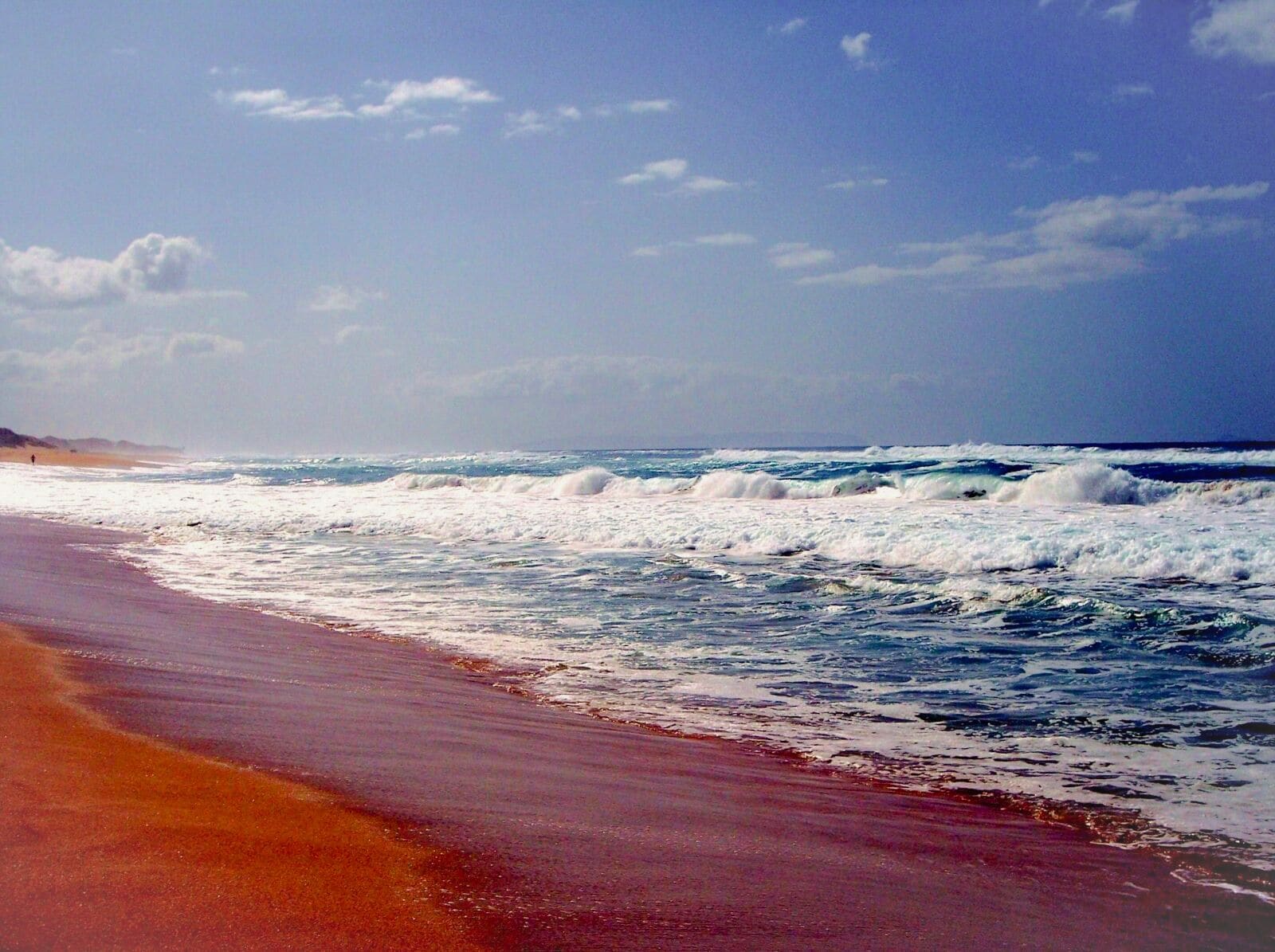 A beach with waves crashing onto the shore under a clear sky.