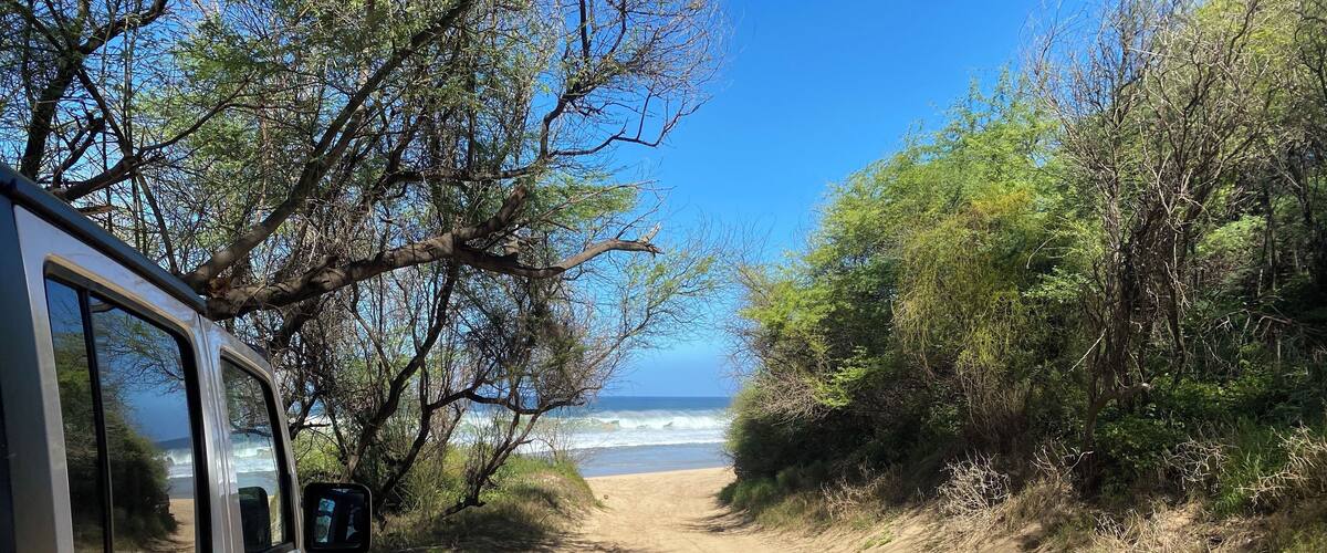 A sandy beach path with a vehicle parked on the left, leading to the ocean.