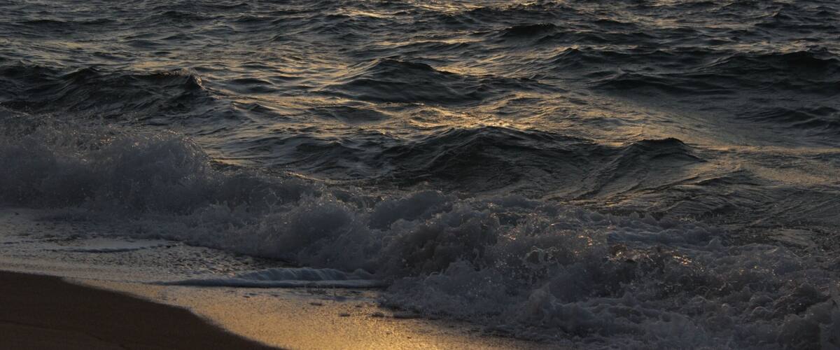 A sunset over the ocean with waves crashing onto the shore.