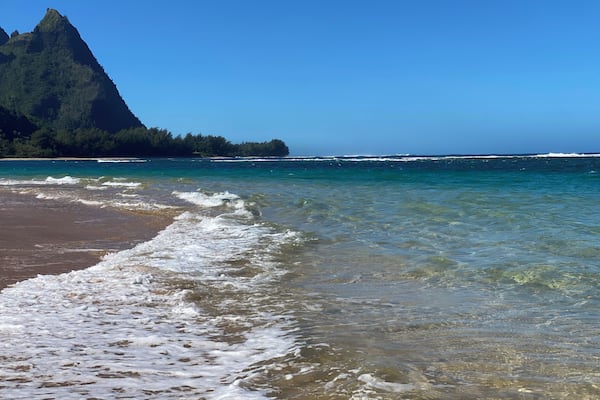 Une plage avec une eau cristalline, des vagues et une montagne en arrière-plan.