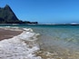 Une plage avec une eau cristalline, des vagues et une montagne en arrière-plan.