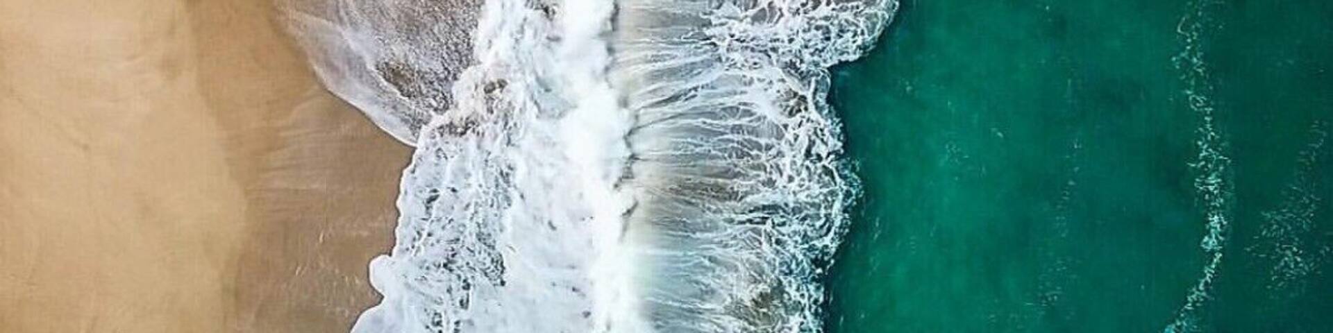 Vista aérea de una playa con aguas turquesas cristalinas y olas blancas rompiendo sobre la orilla.