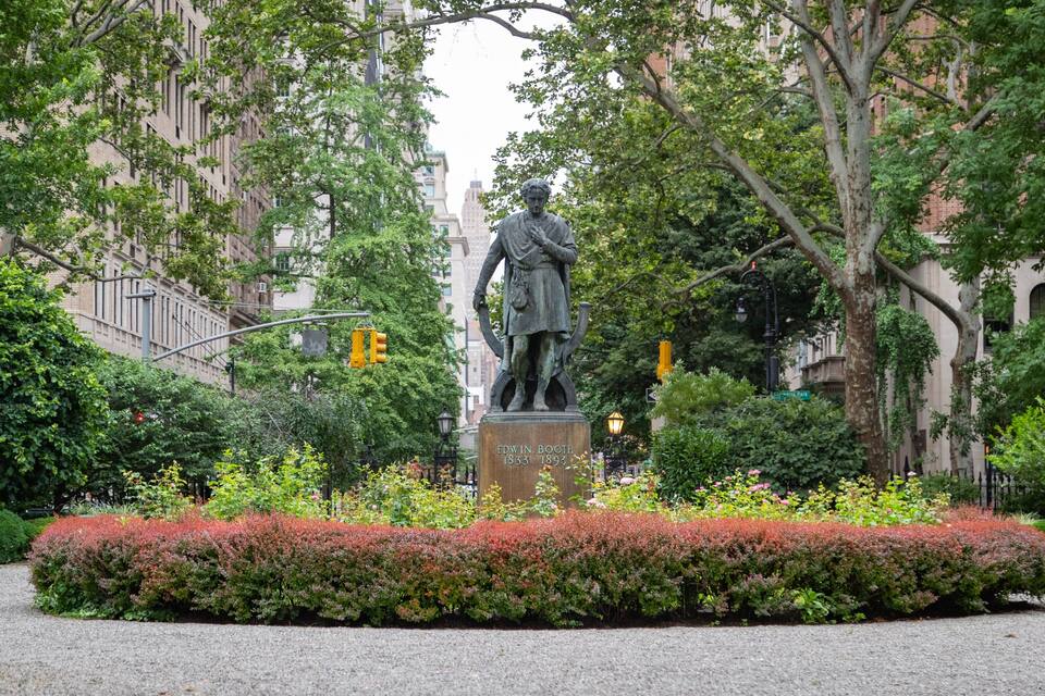 En staty av Edwin Booth i en park omgiven av träd och rött höstlöv.