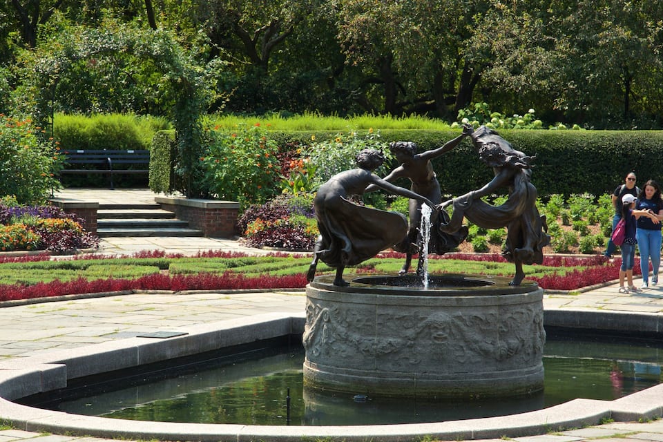 En bronzestatue af to figurer, der leger med en springvand i en have.