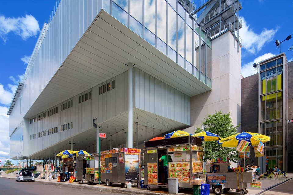 A modern building with a large overhang and food stalls with umbrellas.