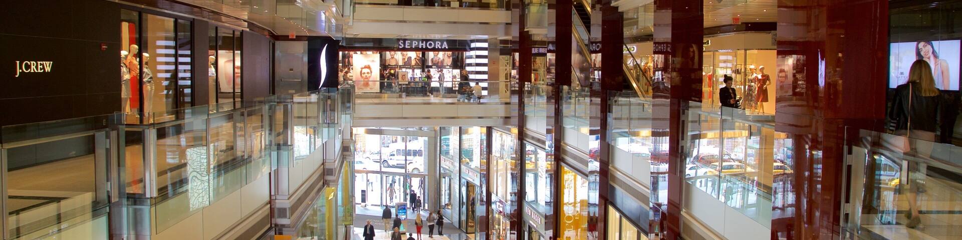 A multi-level shopping mall with glass railings, various stores, and people walking.