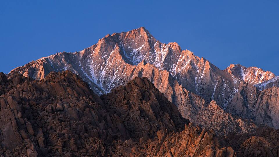 A rugged mountain range with sharp peaks and snow patches.