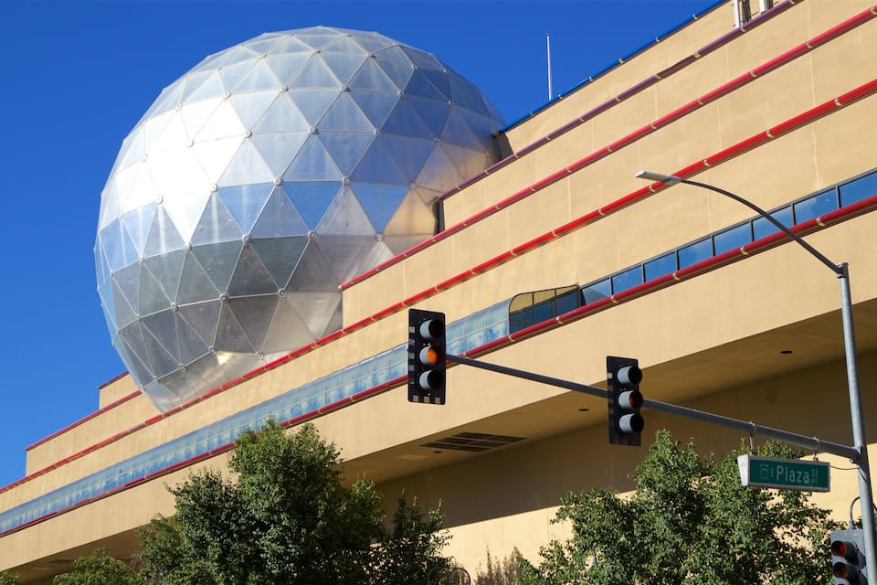 A large geodesic dome structure atop a multi-story building with red and blue glass panels, traffic lights, and a street sign reading "CE Plaza St."