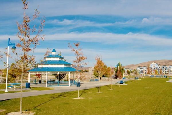 A gazebo with a blue roof, a park with benches, and a building with blue windows in the background.