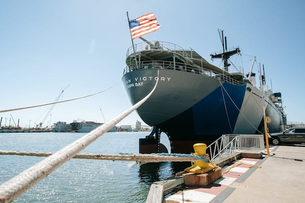 Un gran barco llamado 'San Victory' atracado en un puerto deportivo con una bandera estadounidense.