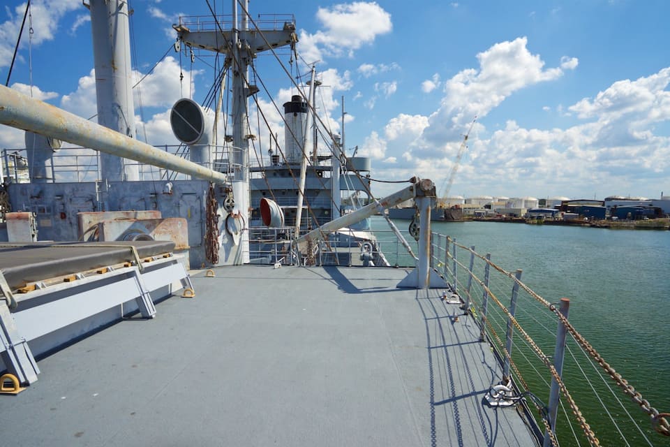 Cubierta de barco con equipo industrial, una grúa y una masa de agua tranquila.