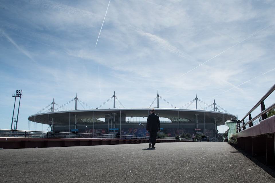 Un homme marchant sur un pont, avec un grand stade en arrière-plan.