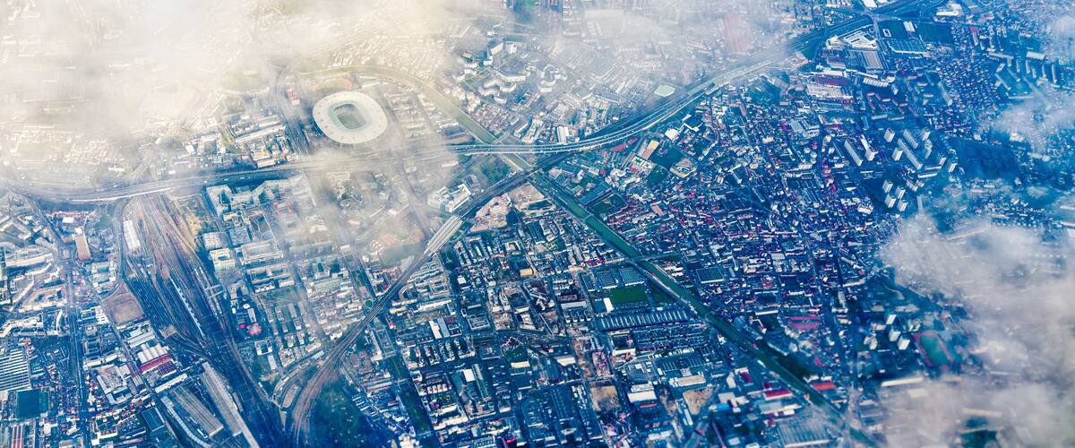 An aerial view of a city with a large stadium, dense urban areas, and a prominent highway.