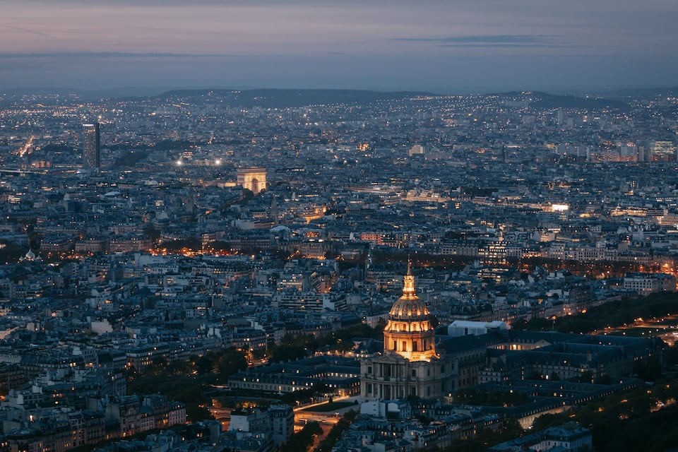 Paisagem urbana ao entardecer, com edifícios iluminados e uma cúpula imponente.