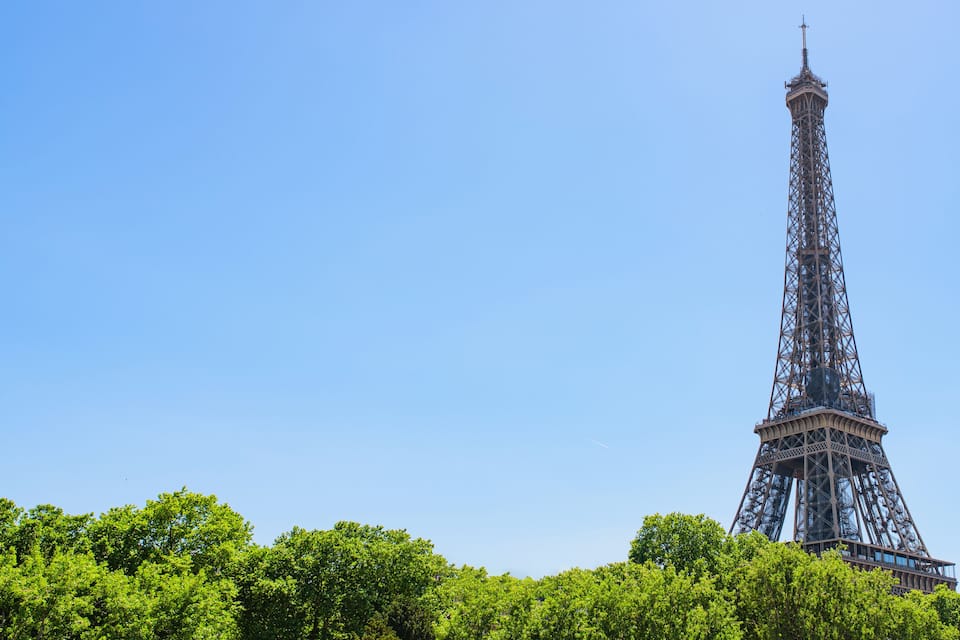 The Eiffel Tower with a clear blue sky and lush green trees in the foreground.