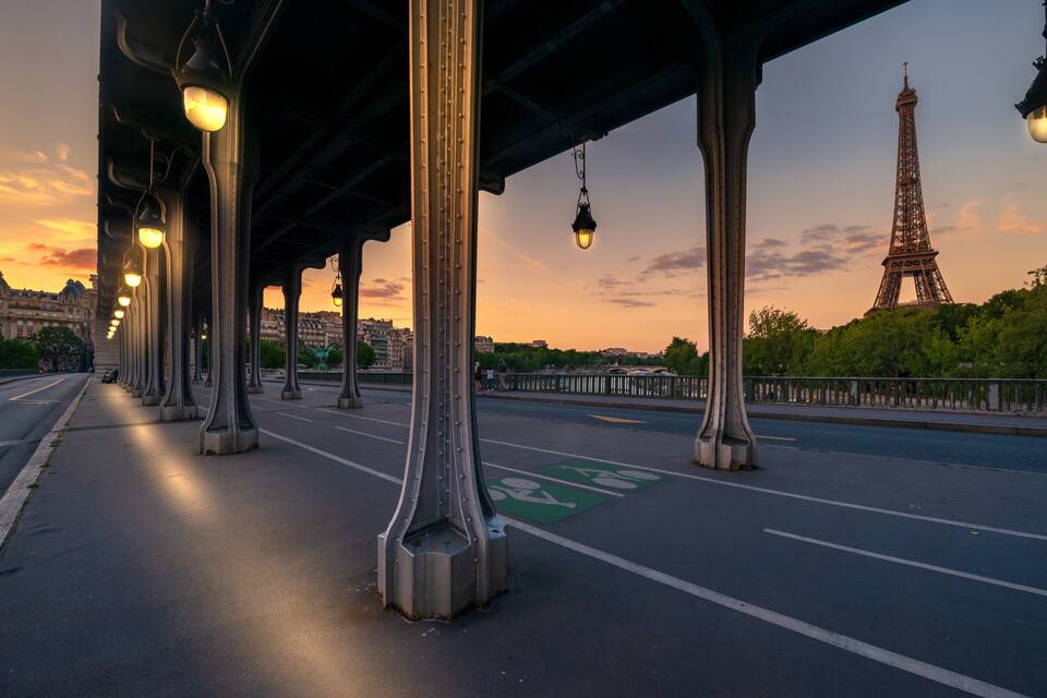 A bridge with street lamps, a green bike lane, and the Eiffel Tower in the background.