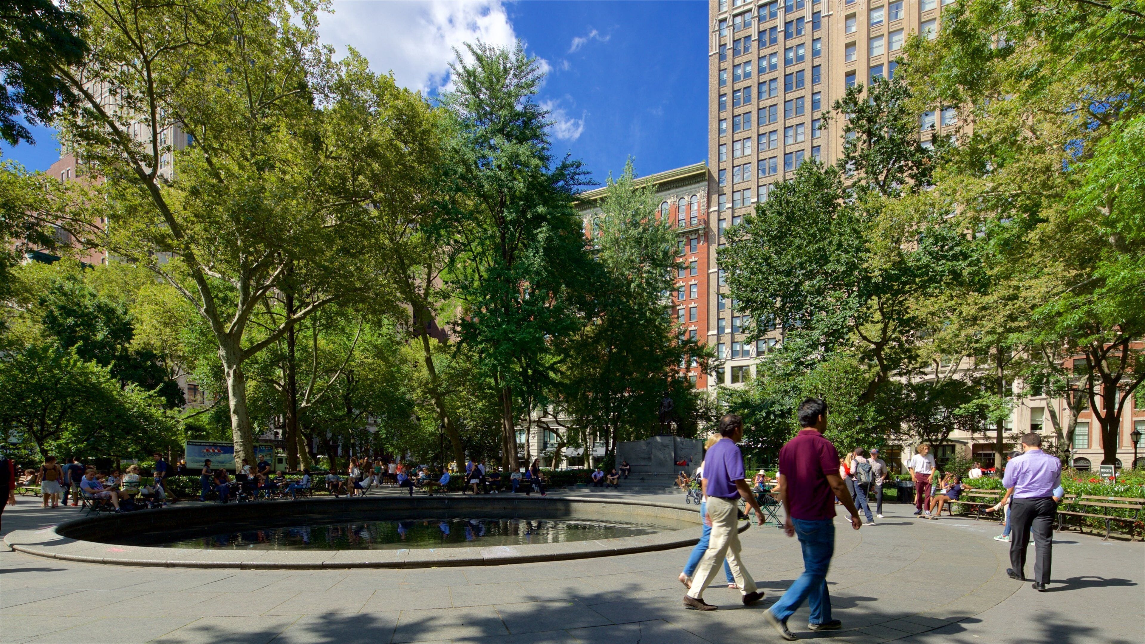 A public square with a fountain, surrounded by trees and buildings.