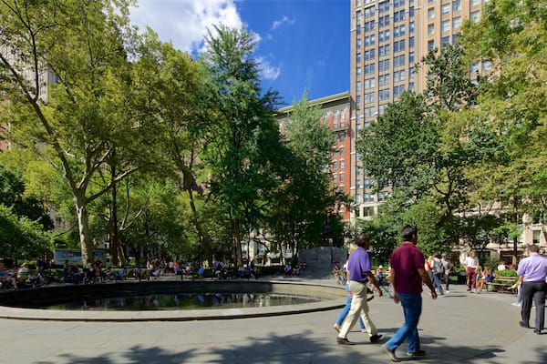 A public square with a fountain, surrounded by trees and buildings.
