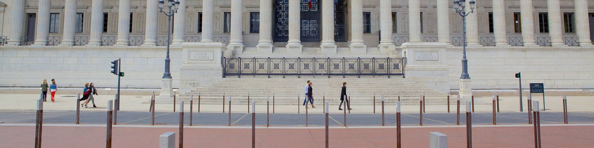 A grand neoclassical building with a central entrance flanked by columns, a clock, and a flag.