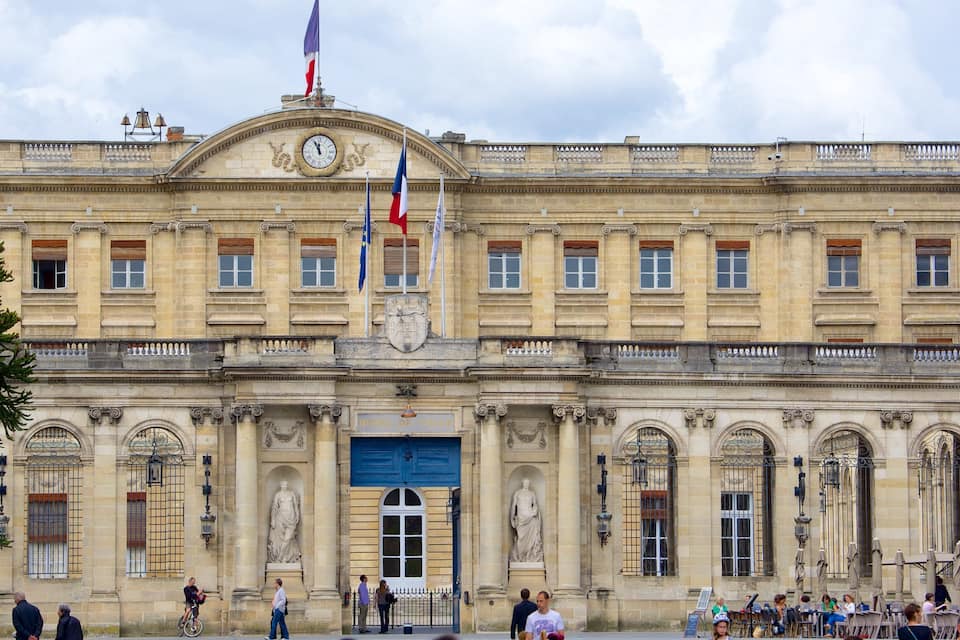A historic building with a large clock, statues, and flags.