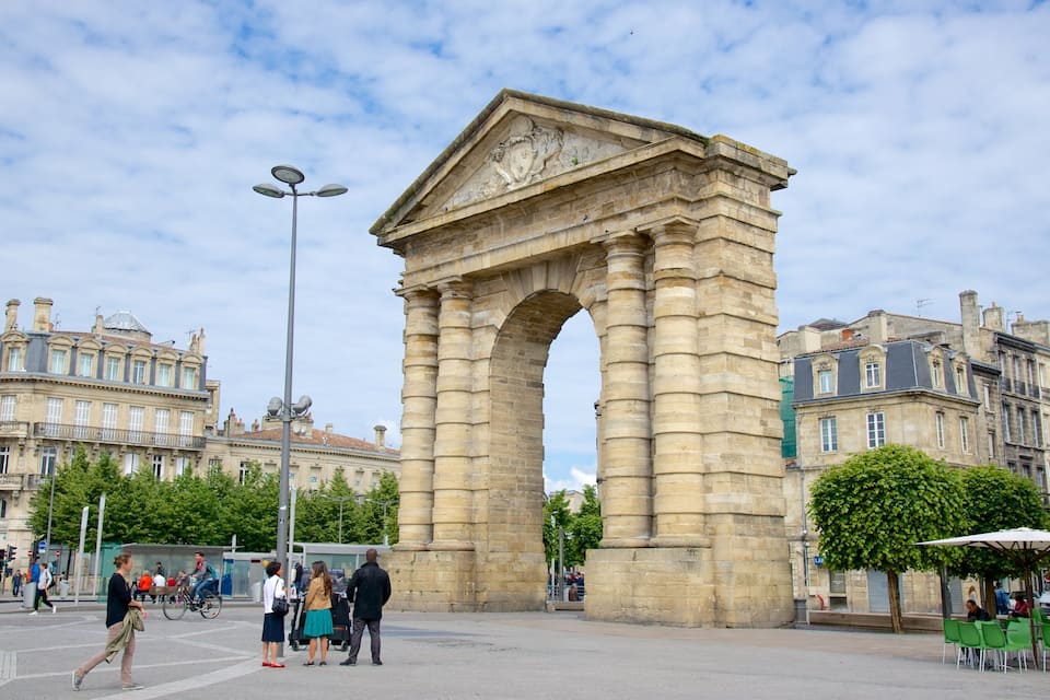 A historic stone archway in a city square with pedestrians and buildings in the background.