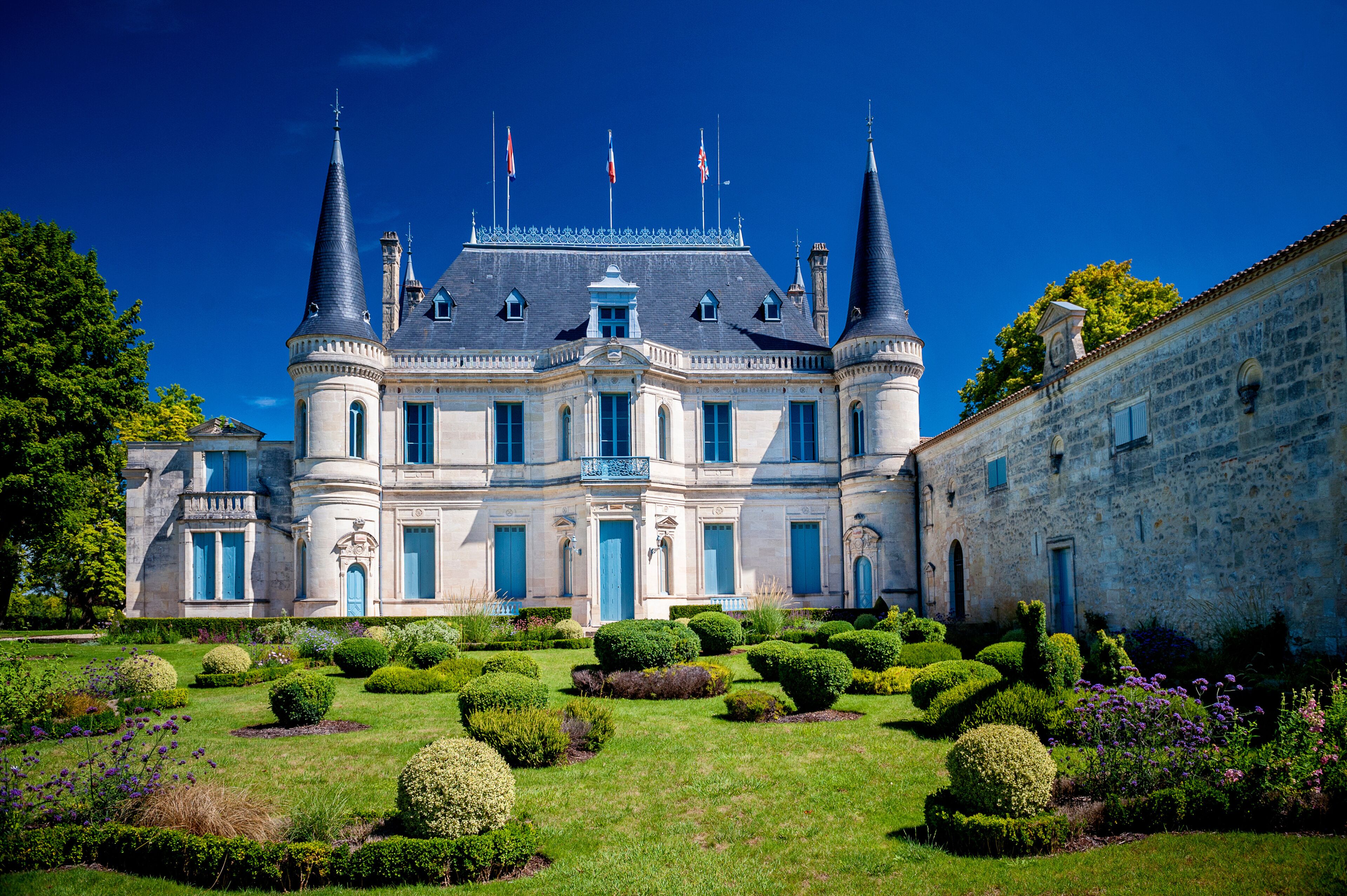 A grand château with two prominent towers, a well-manicured garden, and a clear blue sky.