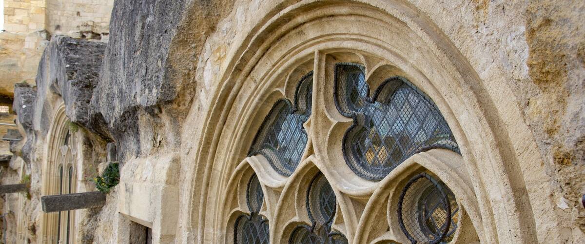 A stone building with a large arched window featuring intricate tracery and a mesh design.