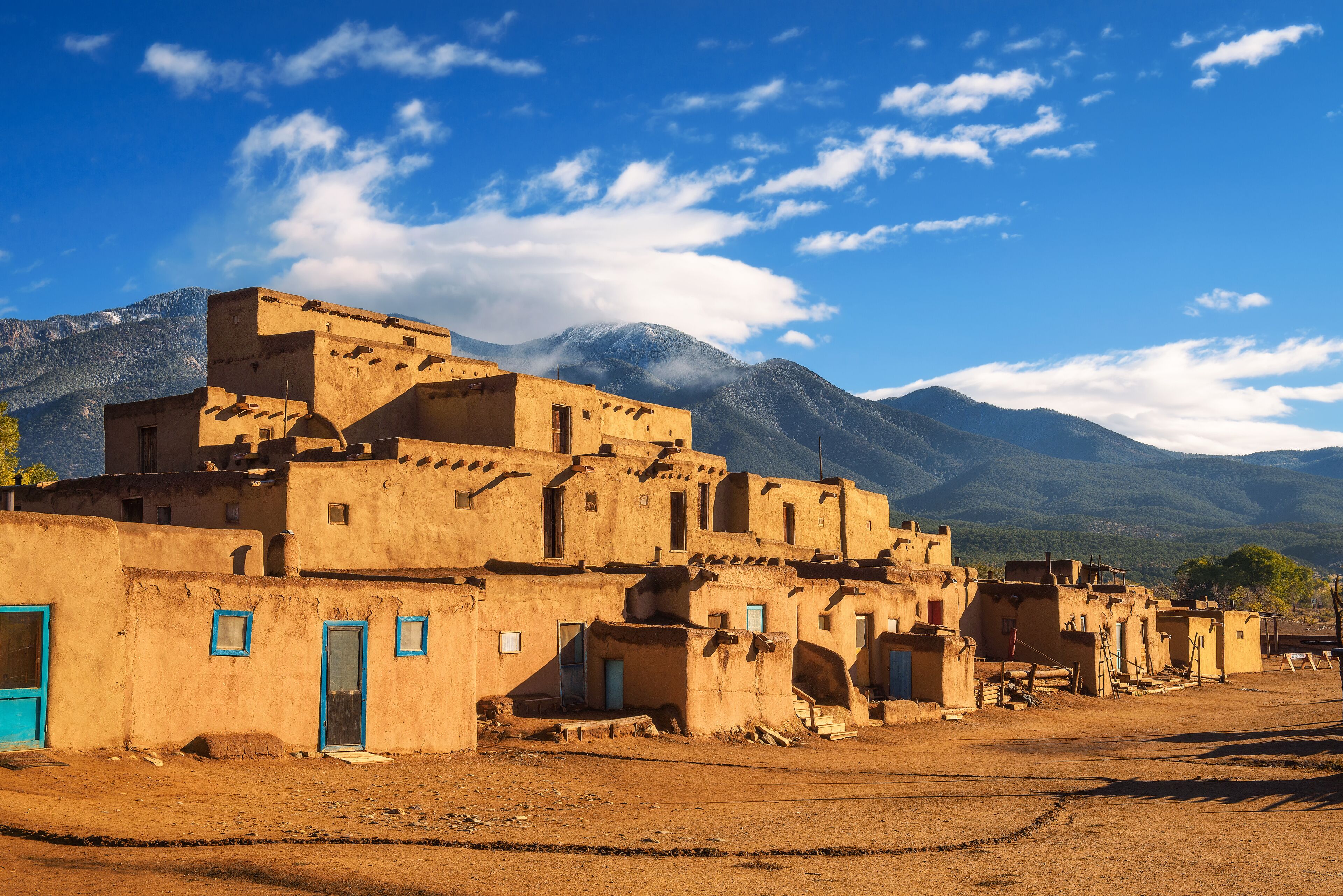 A village with adobe buildings, a clear sky, and mountains in the background.