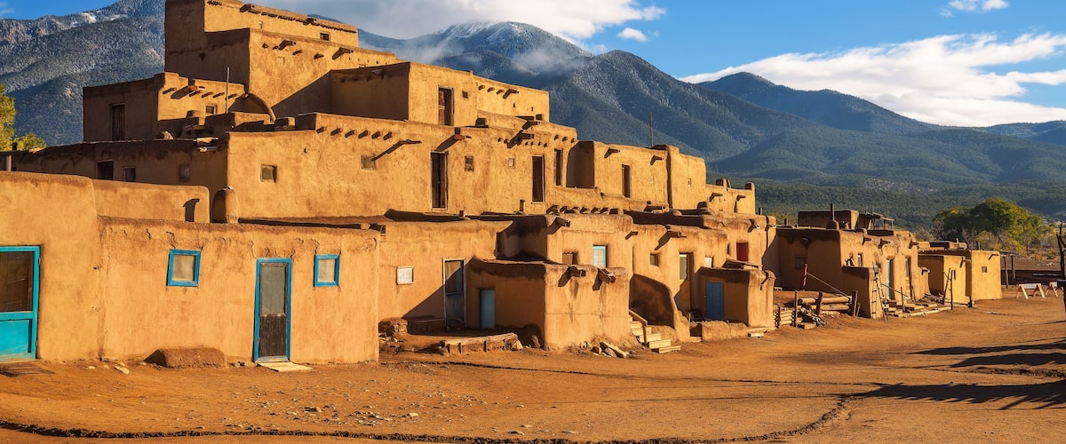 A village with adobe buildings, a clear sky, and mountains in the background.