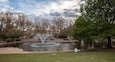 A park with a fountain, trees, and a pond.
