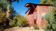 A rustic red barn with a 'Produce Processing' sign, surrounded by trees and a dirt path.