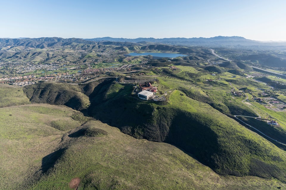 A mountainous landscape with a town nestled in a valley, a large body of water, and a prominent building on a hill.
