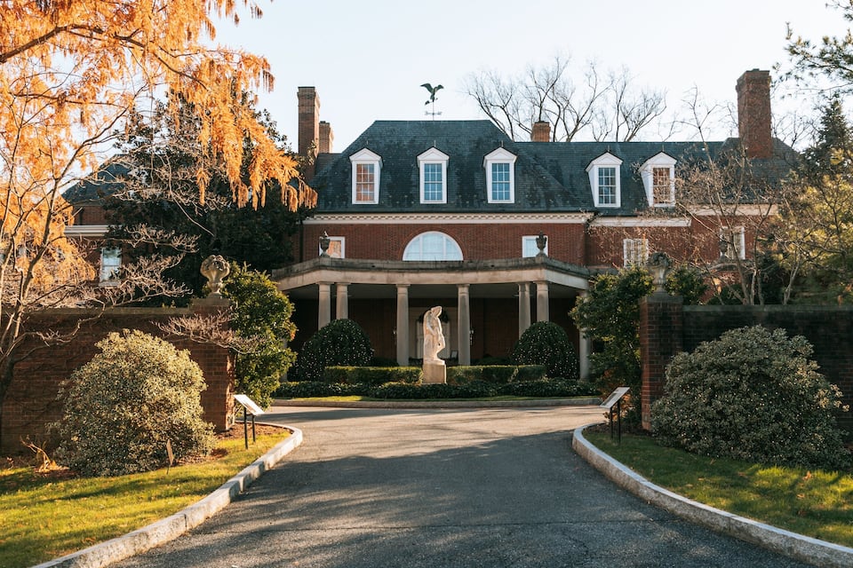 A large brick mansion with a central portico, surrounded by well-maintained lawns and trees.