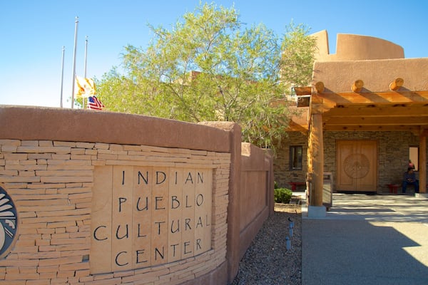 Das Indian Pueblo Cultural Center mit einer Steinmauer, einer US-amerikanischen Flagge und einer Holzbauten mit einem kreisförmigen Emblem.