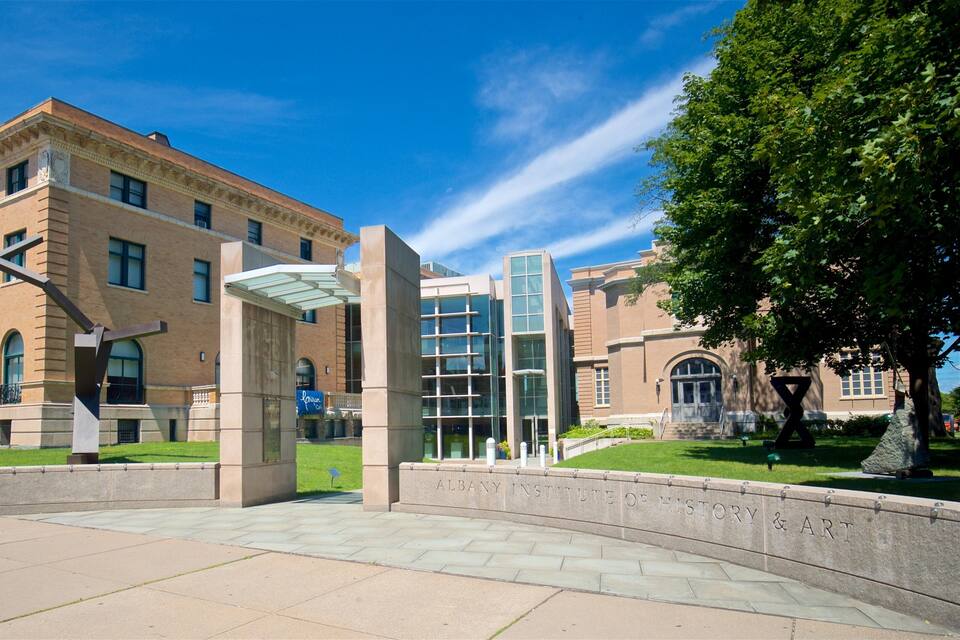 A historic building with a large banner, a modern glass structure, and a well-maintained lawn.