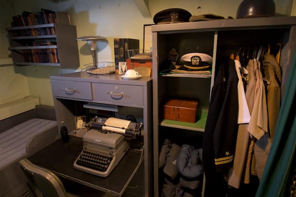 Ein stilvolles Büro mit Schreibmaschine, Bücherregalen und einem Kleiderständer mit Hüten.