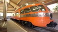Ein orangefarbener Zug mit der Aufschrift 'Hawatha' auf der Vorderseite, geparkt an einem Bahnhof mit hölzernen Bänken und gefliestem Boden.