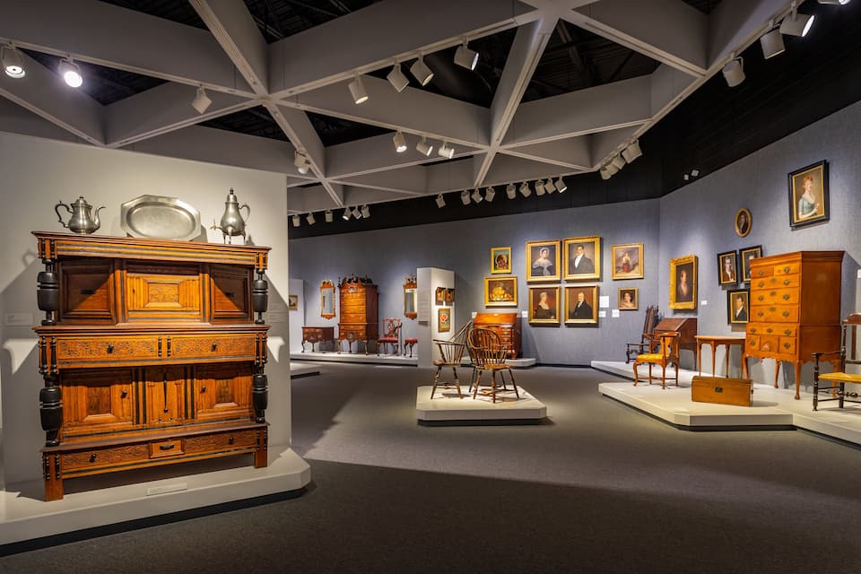 An interior exhibition space with antique furniture and framed portraits.