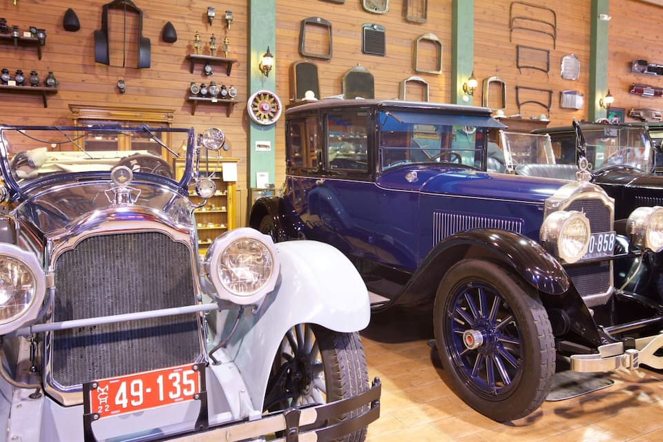 Vintage cars in a museum with wooden walls and various antique items displayed.