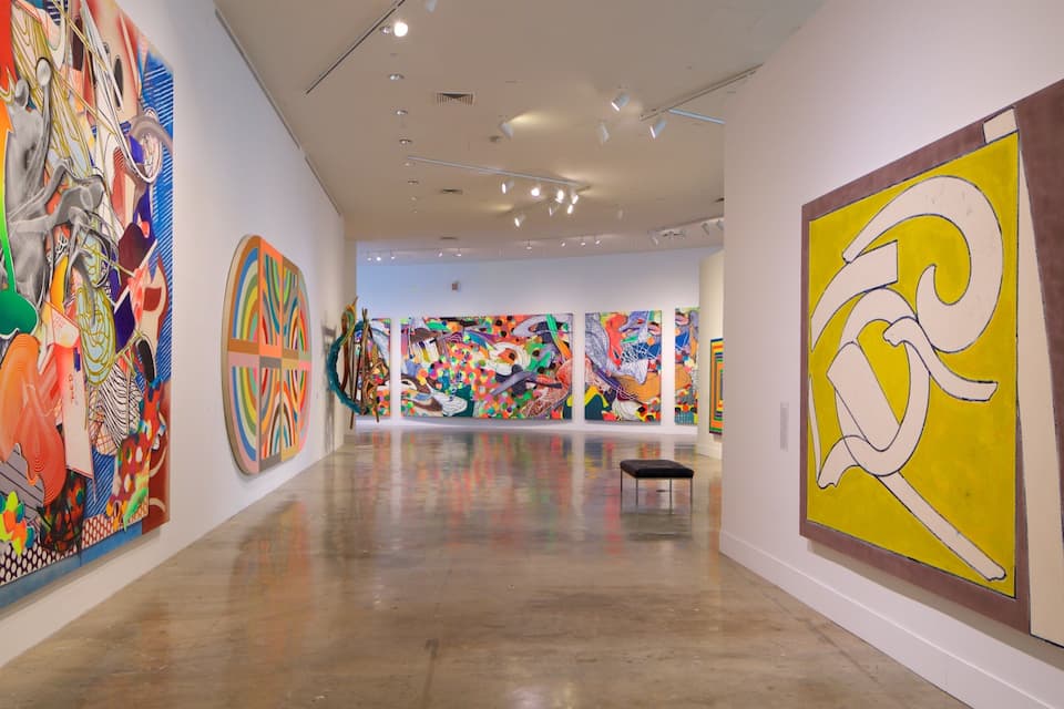Een kunstgalerie met kleurrijke abstracte schilderijen aan de muur.