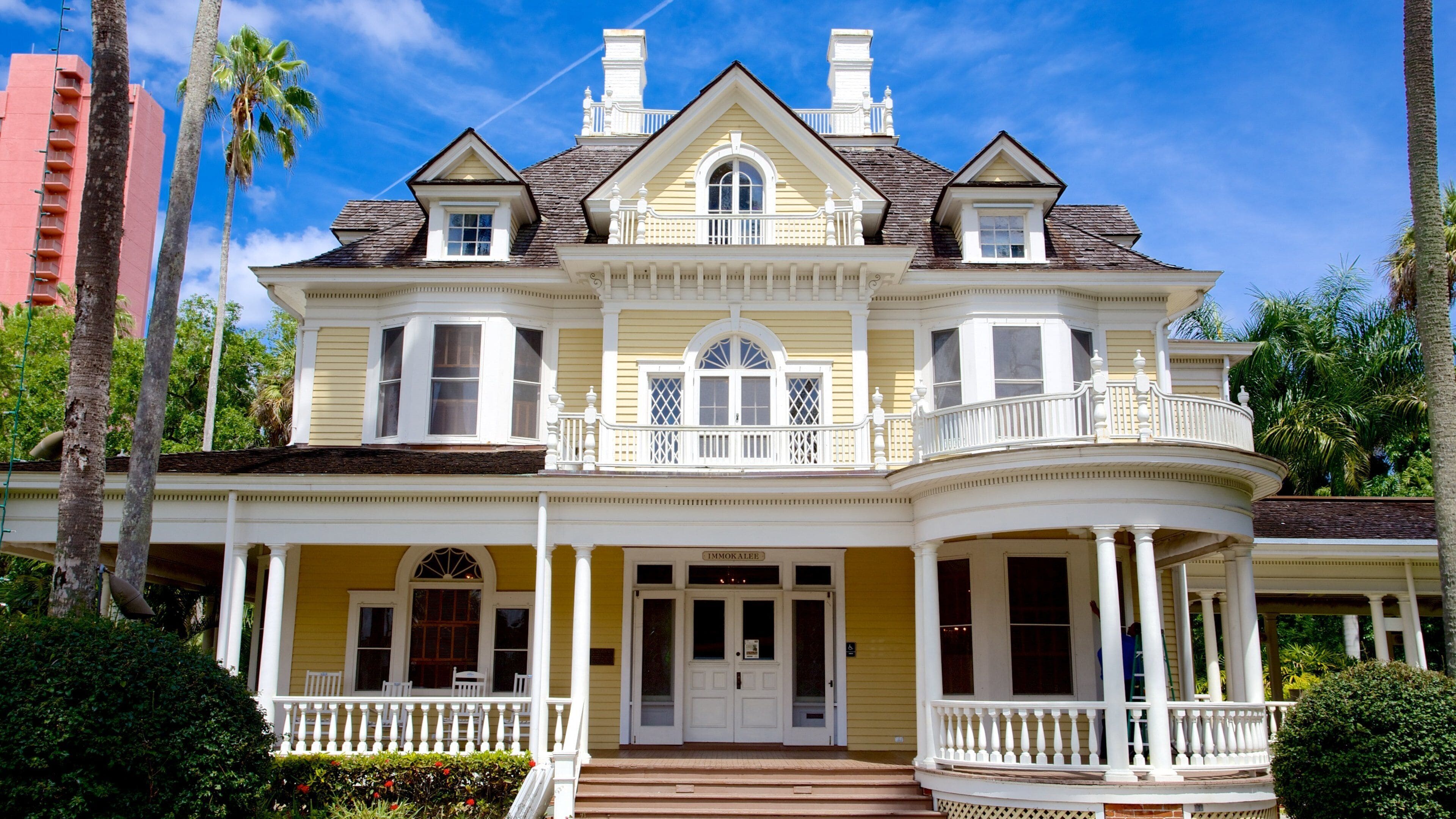 A large, yellow Victorian-style house with a wrap-around porch, multiple windows, and a balcony.