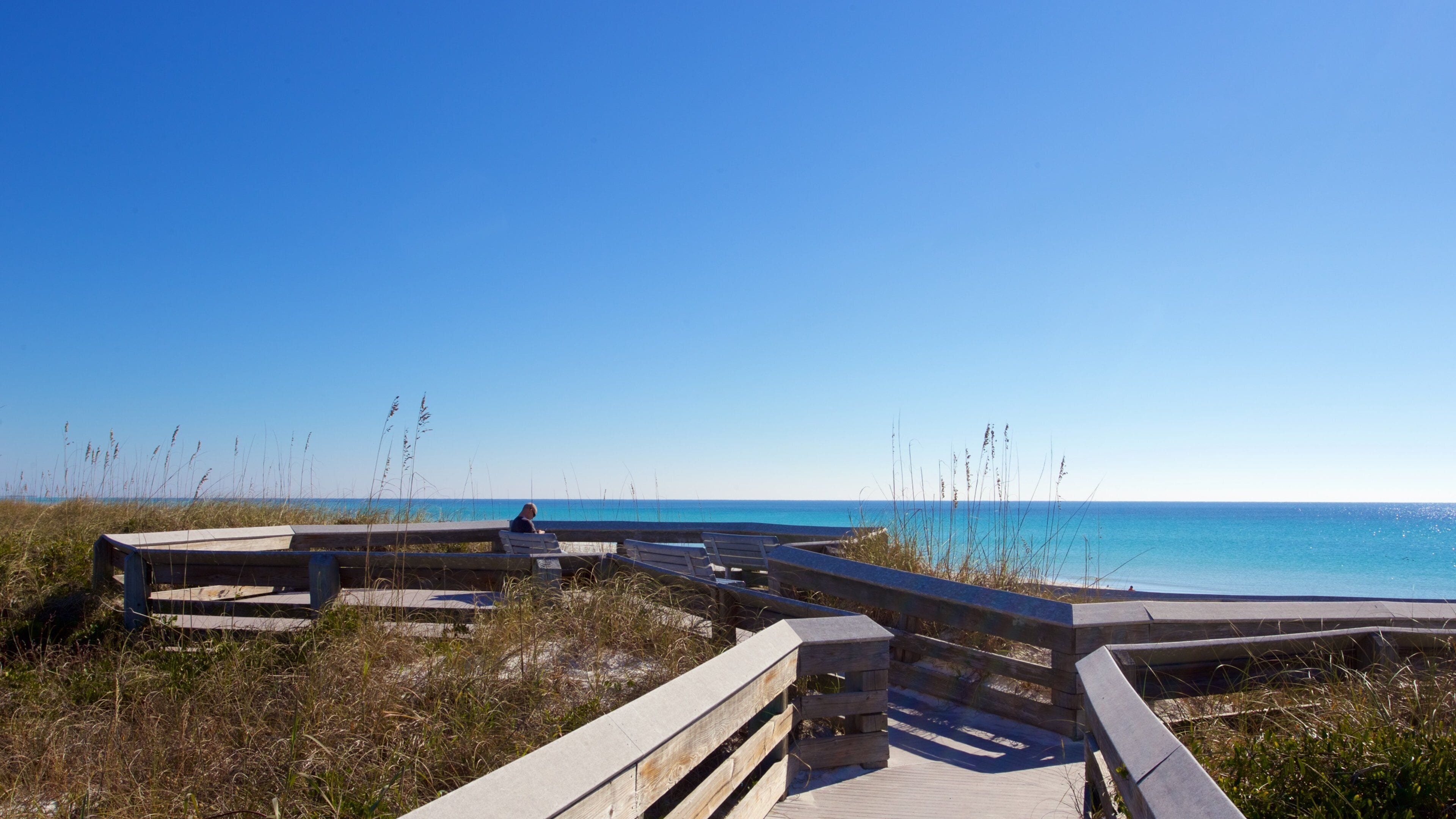 A wooden boardwalk leading to a beach with clear blue water and a clear sky.