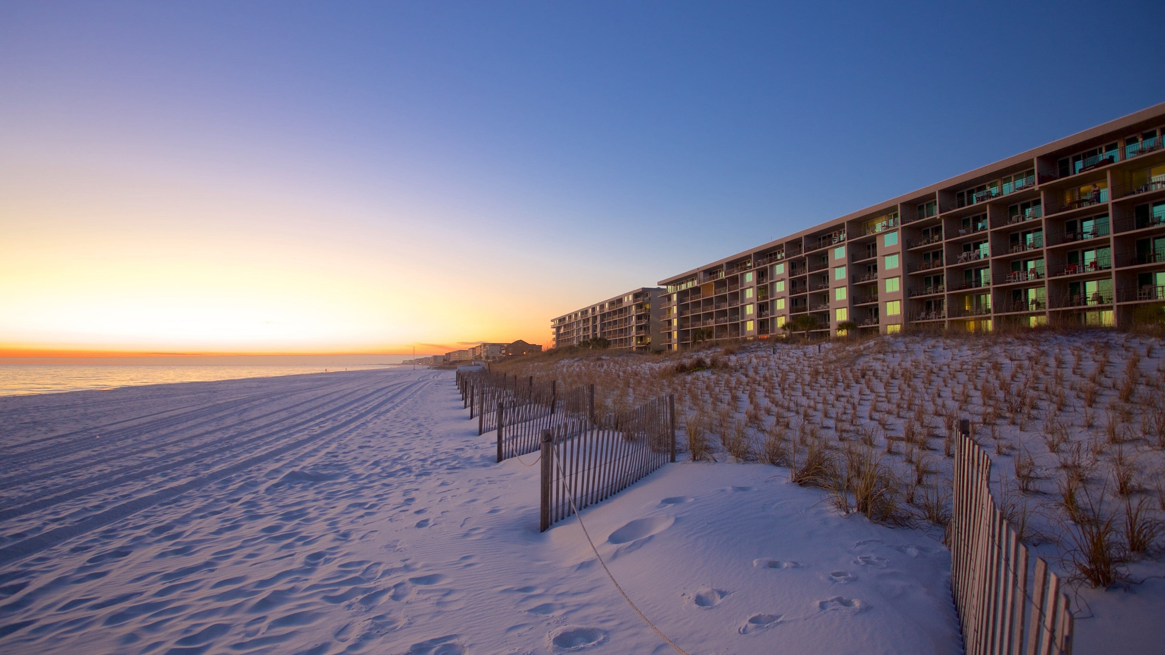 A snow-covered beach at sunset with a hotel in the background.